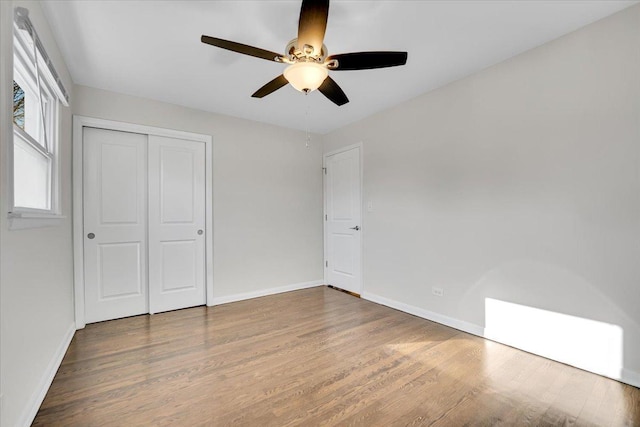 unfurnished bedroom featuring a closet, baseboards, wood finished floors, and a ceiling fan