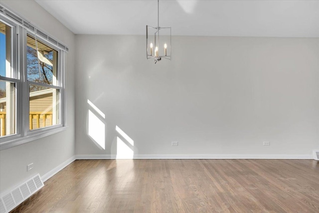 unfurnished room with visible vents, baseboards, wood finished floors, and a chandelier