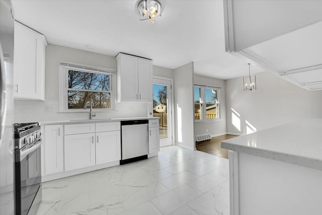 kitchen with a sink, stainless steel appliances, light countertops, marble finish floor, and backsplash