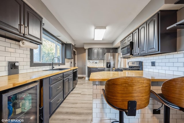 kitchen featuring tasteful backsplash, wine cooler, butcher block counters, stainless steel appliances, and a sink