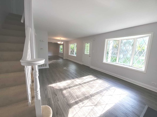 unfurnished living room featuring stairway, baseboards, a notable chandelier, and dark wood-style flooring