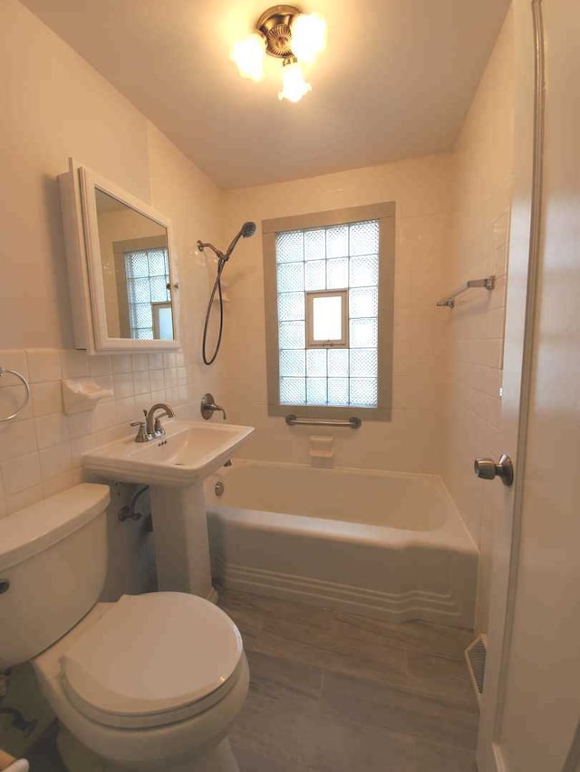 full bathroom with a wealth of natural light, toilet, tile walls, and shower / bathtub combination