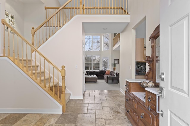 entryway featuring baseboards, a high ceiling, stone tile floors, and stairs