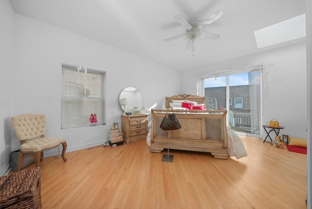 bedroom with access to exterior, baseboards, light wood-type flooring, a skylight, and a ceiling fan