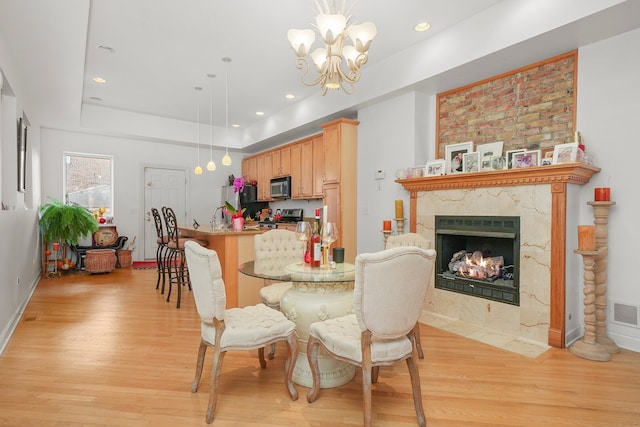 dining space featuring a tray ceiling, a premium fireplace, light wood-type flooring, and a chandelier