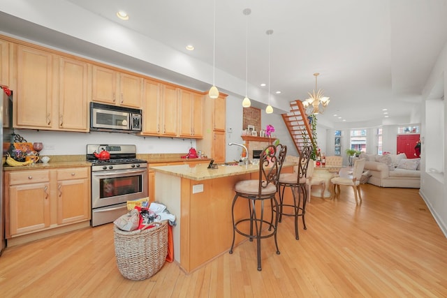 kitchen with light brown cabinets, a notable chandelier, light wood-style flooring, and appliances with stainless steel finishes