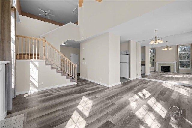 unfurnished living room with stairway, wood finished floors, baseboards, a fireplace, and ceiling fan with notable chandelier