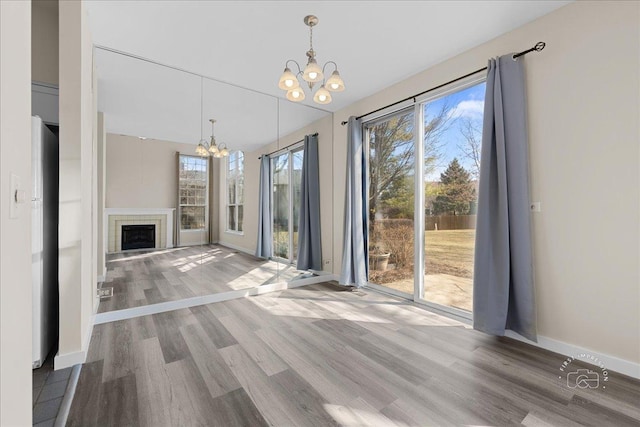 unfurnished living room with baseboards, wood finished floors, a chandelier, and a fireplace