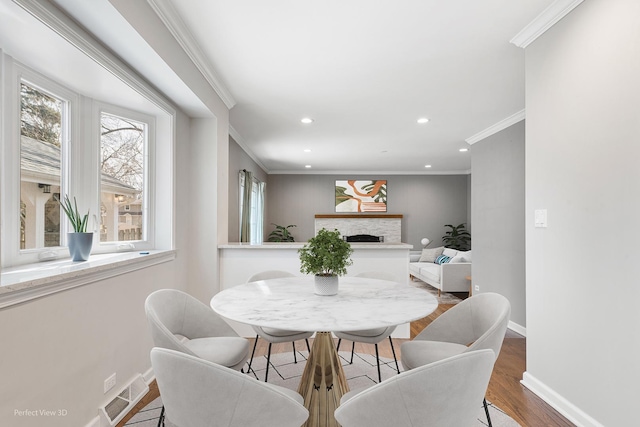 dining area featuring visible vents, crown molding, baseboards, a fireplace, and wood finished floors