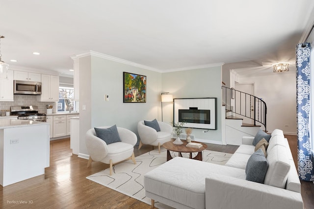 living area featuring a glass covered fireplace, crown molding, stairs, and wood finished floors