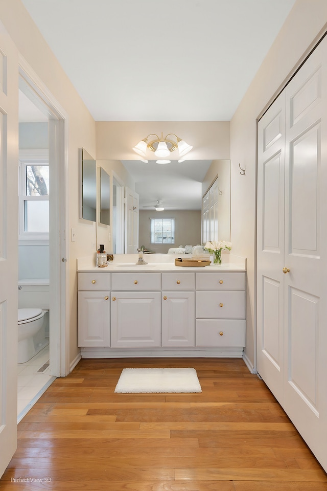 bathroom with vanity, wood finished floors, baseboards, a ceiling fan, and toilet