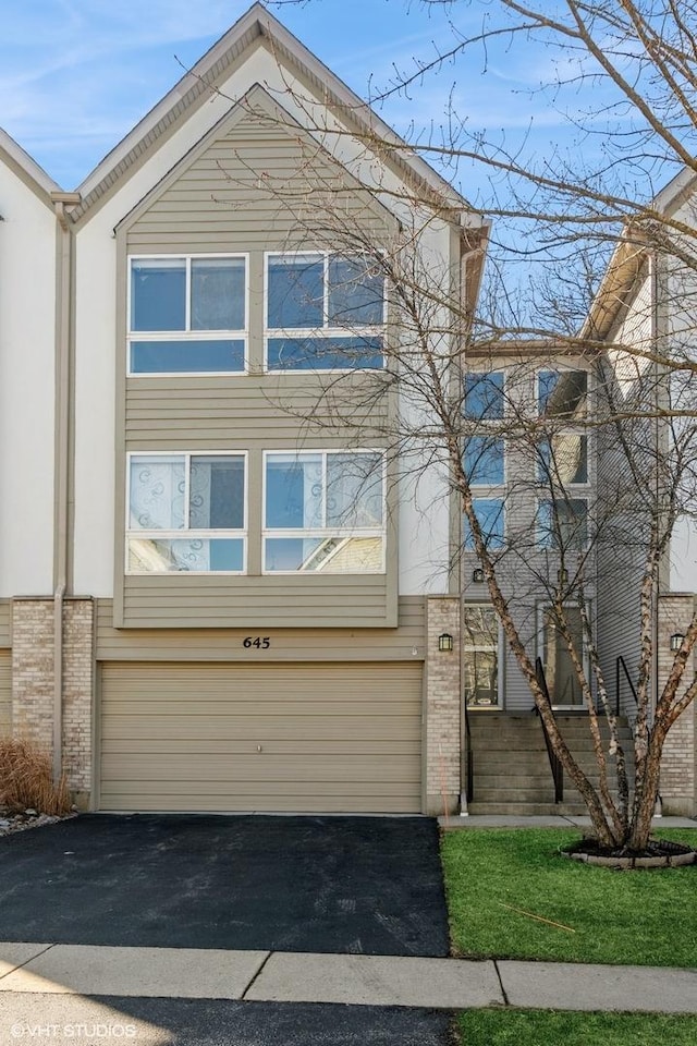 townhome / multi-family property featuring aphalt driveway, brick siding, and an attached garage