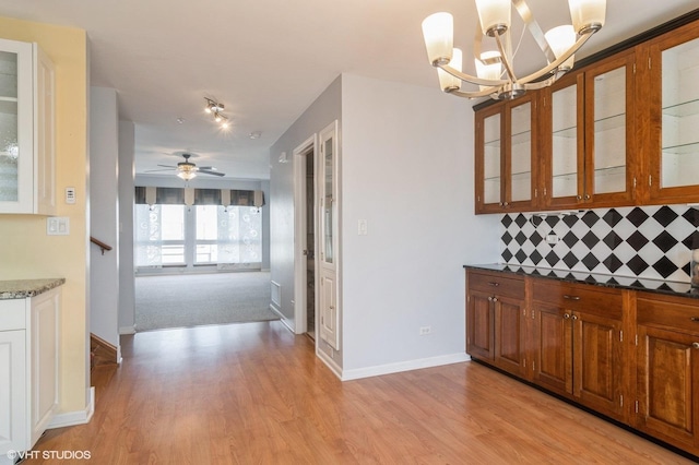 kitchen featuring brown cabinetry, baseboards, light wood-style flooring, glass insert cabinets, and tasteful backsplash