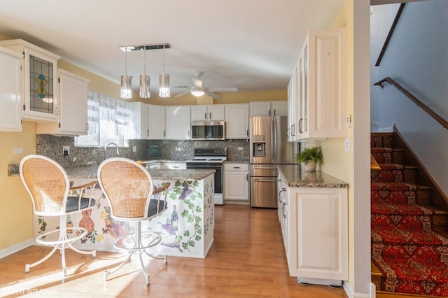 kitchen featuring stone countertops, appliances with stainless steel finishes, white cabinets, decorative backsplash, and hanging light fixtures