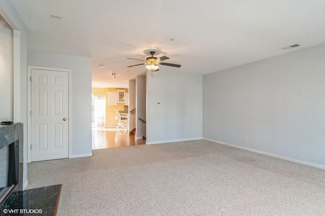 unfurnished living room with visible vents, baseboards, a fireplace with flush hearth, ceiling fan, and carpet flooring