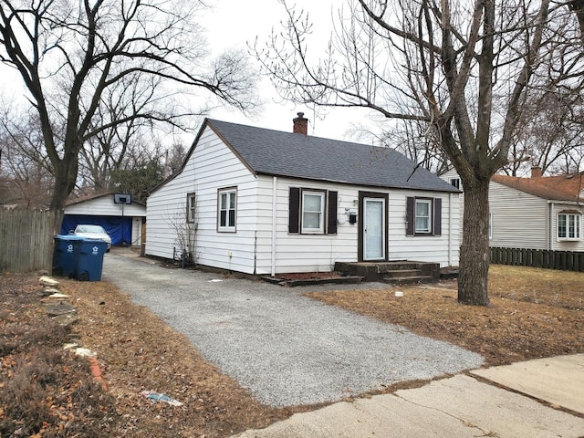 view of front of home featuring an outbuilding, driveway, fence, roof with shingles, and a chimney