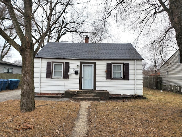 bungalow-style house with fence, roof with shingles, and a chimney