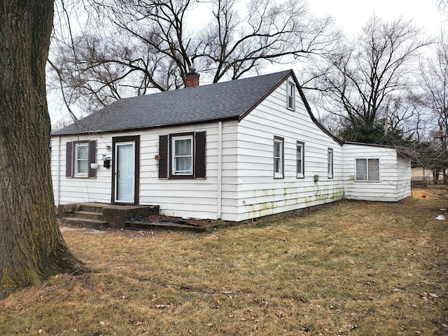 view of front facade with a chimney, a front yard, and roof with shingles