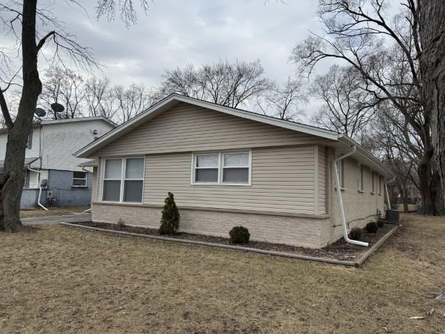 view of side of property with brick siding, central air condition unit, and a lawn