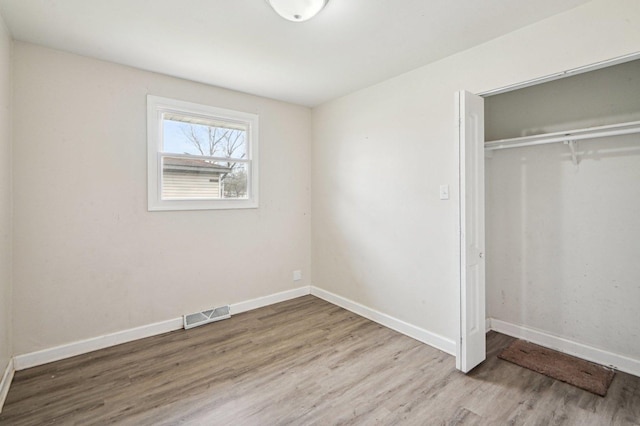 unfurnished bedroom featuring baseboards, wood finished floors, visible vents, and a closet