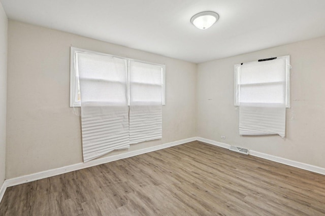 spare room with baseboards, wood finished floors, visible vents, and a wealth of natural light