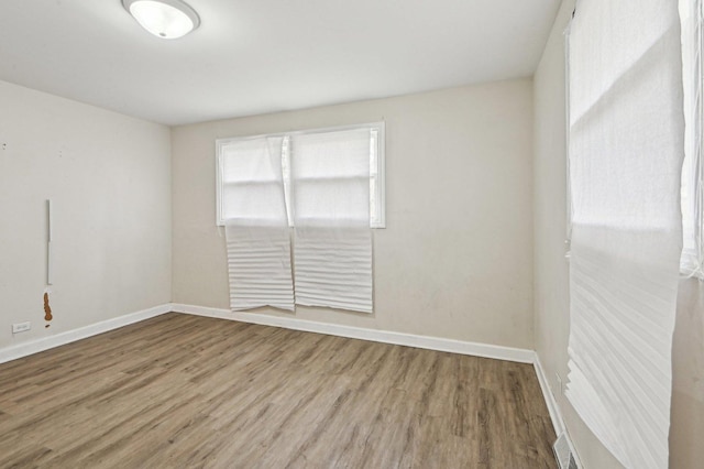 empty room with wood finished floors, visible vents, and baseboards