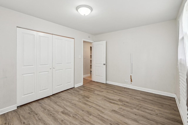 unfurnished bedroom featuring baseboards, wood finished floors, and a closet