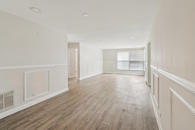 spare room with a decorative wall, a wainscoted wall, visible vents, and light wood-type flooring