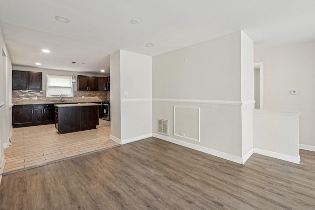 kitchen with dark brown cabinets, visible vents, a sink, light wood-type flooring, and a center island