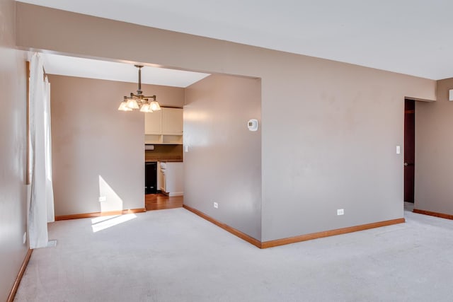 empty room featuring light colored carpet, baseboards, and a chandelier