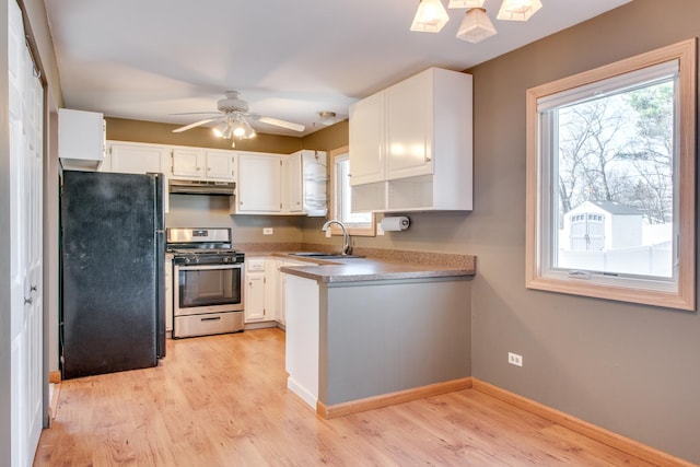 kitchen with under cabinet range hood, freestanding refrigerator, light wood-style floors, stainless steel gas range, and a sink