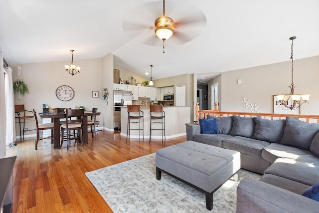 living area with light wood finished floors, ceiling fan with notable chandelier, baseboards, and lofted ceiling