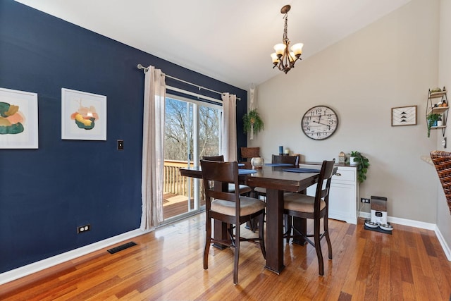 dining space featuring visible vents, baseboards, vaulted ceiling, wood finished floors, and a notable chandelier