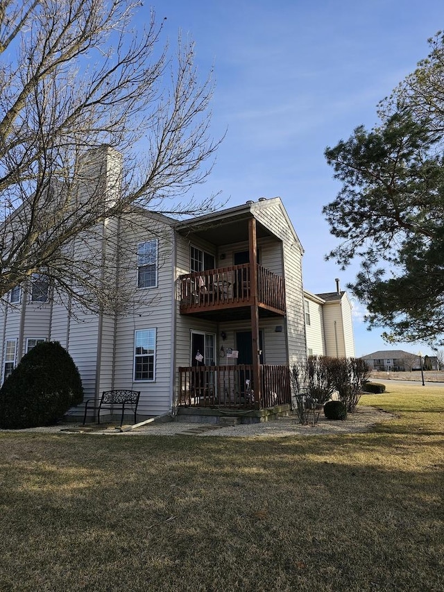 rear view of property featuring a balcony, a yard, and a chimney