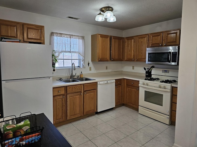 kitchen with brown cabinetry, visible vents, white appliances, and a sink