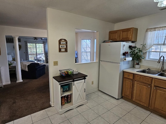 kitchen featuring brown cabinets, light carpet, a sink, freestanding refrigerator, and light tile patterned flooring