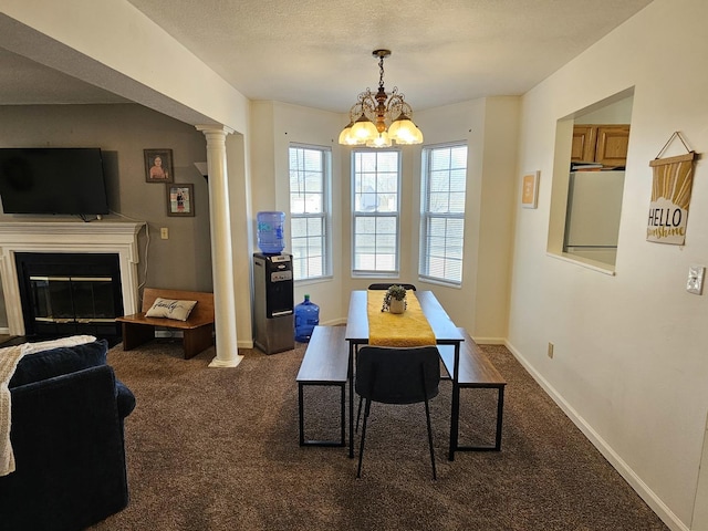 dining room featuring baseboards, dark carpet, a glass covered fireplace, a textured ceiling, and ornate columns