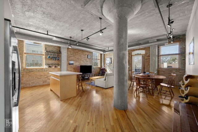 living area featuring ornate columns, brick wall, rail lighting, and light wood finished floors