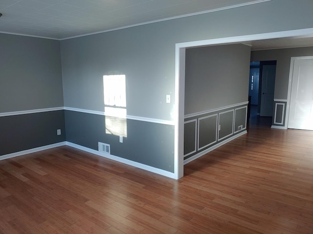 empty room with visible vents, ornamental molding, a decorative wall, and wood finished floors