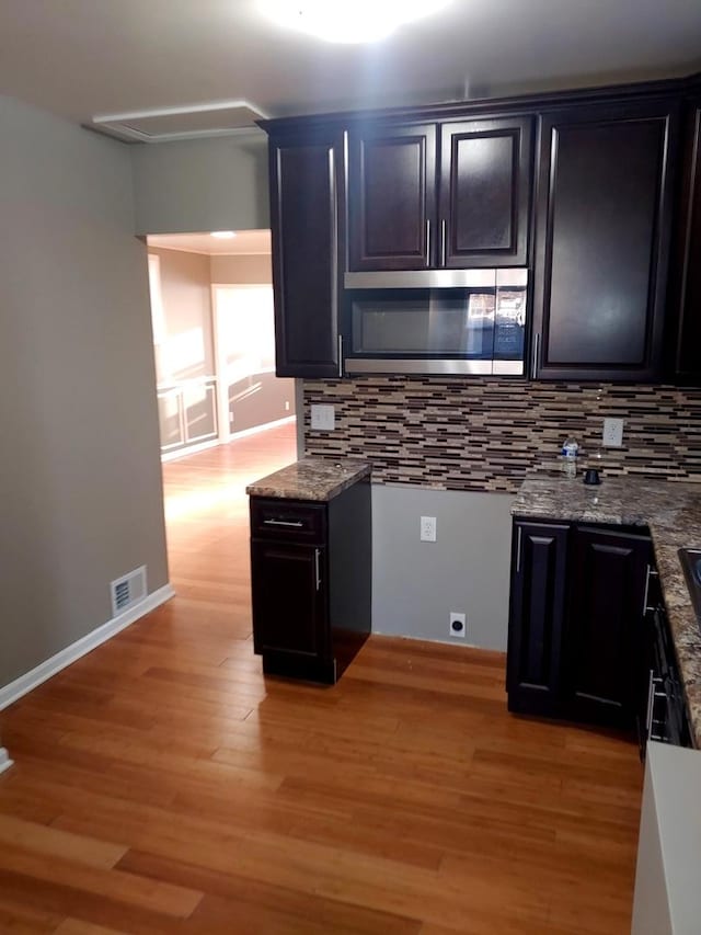 kitchen with visible vents, stainless steel microwave, light wood-style floors, decorative backsplash, and baseboards