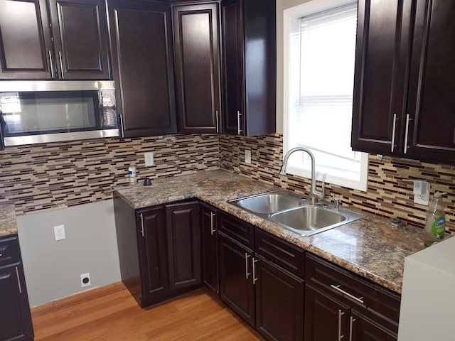 kitchen with stainless steel microwave, light wood-style floors, tasteful backsplash, and a sink