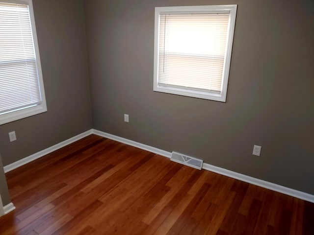 unfurnished room featuring a wealth of natural light, visible vents, baseboards, and wood finished floors