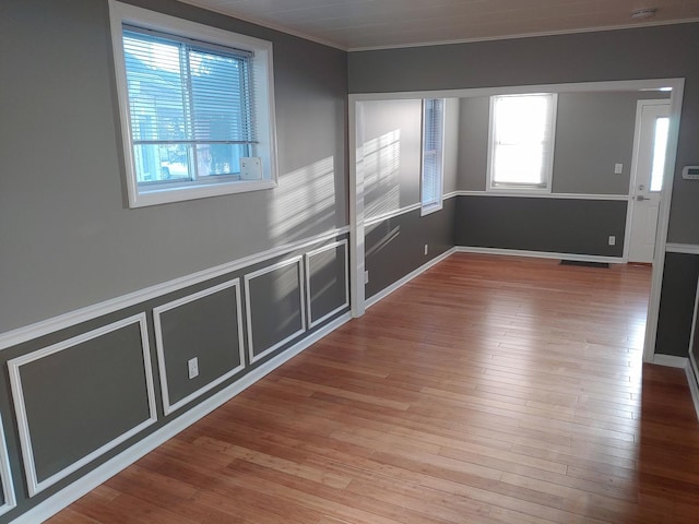 empty room featuring a wainscoted wall, a decorative wall, ornamental molding, and hardwood / wood-style flooring