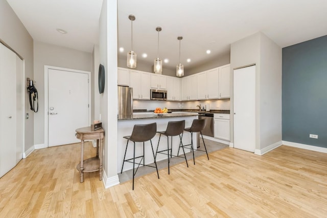 kitchen featuring light wood-type flooring, a kitchen bar, appliances with stainless steel finishes, hanging light fixtures, and white cabinetry