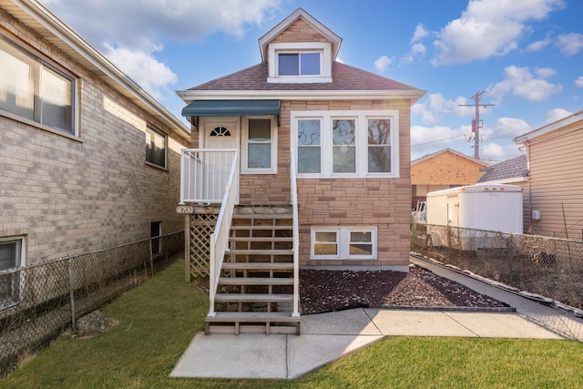 rear view of house with stone siding, fence, a yard, a shingled roof, and stairs