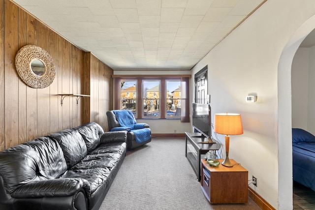 carpeted living area featuring baseboards, arched walkways, and wood walls