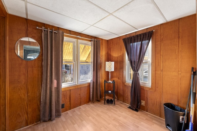 interior space with a wealth of natural light, a drop ceiling, wood walls, and light wood-style flooring