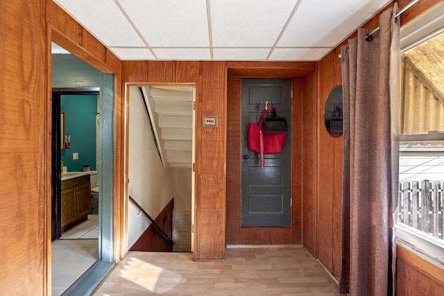 corridor featuring light wood-type flooring, a paneled ceiling, and wooden walls