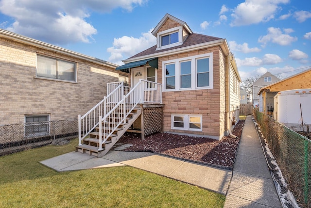 view of front facade featuring stone siding, a front yard, and fence