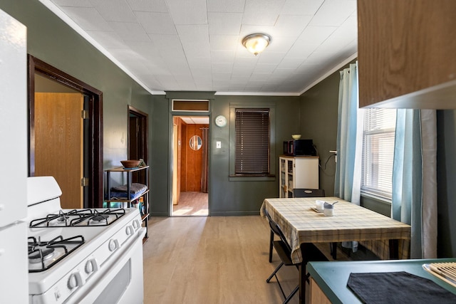 kitchen featuring white range with gas cooktop, light wood-style floors, baseboards, and ornamental molding